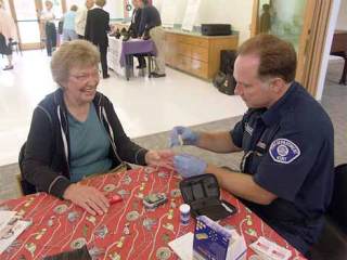 Kent firefighter John Robbins entertains a resident while checking her blood-sugar levels at the Kent Senior Activity Center.