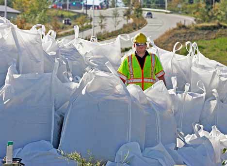 City maintenance worker Matt McCullough stands in a pile of sand bags and guides them into place Tuesday at the end of River View Drive