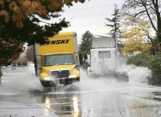 Trucks drive through a flooded 76th Street in Kent