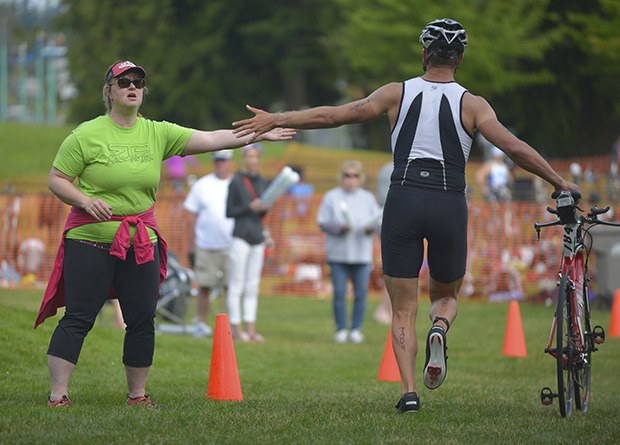 Dave Preston grabs a high-five from a bystander as he walks his bike into the gear exchange point of the Lake Meridian Triathlon last Sunday.