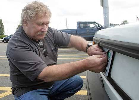 Dave George of Kent places his tabs on his car outside the Kent Licensing Agency Office Tuesday. While he doesn’t like the idea of added fees
