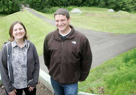 City of Kent Visual Arts Coordinator Cheryl dos Remédios and Park Project Manager Brian Levenhagen pose with Earthworks Park's split rings behind them June 17. The split rings will be restored with $70
