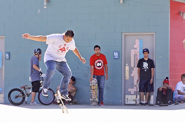 Ronnie Gerona performs a kickflip while his friends look on from a cooler position in the shade at Arbor Heights 360 Skate Park in Kent on Tuesday.