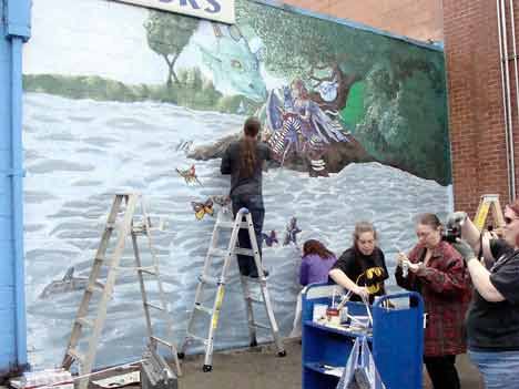 A local group of helpers works on a revamped mural for Browser’s New and Used Books in downtown Kent