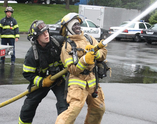 Kent-Meridian senior Simon Okullu receives fire hose training from firefighter Jesse Wise.