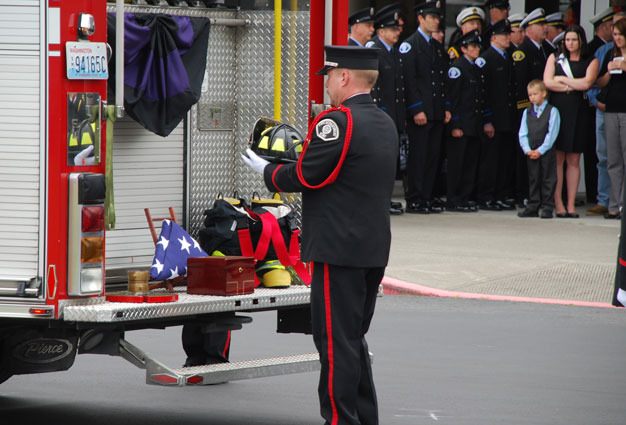 Honor guard member Chris Lindahl places the helmet of Kent firefighter Ernie Rideout on the tailboard of Fire Engine 71 alongside his ashes as firefighters stand at attention at a service for Rideout June 14 at River of Life Church in Kent.