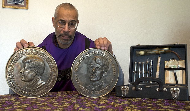 Marcus Shelton holds up memorial discs given to his father who was assigned to John F. Kennedy’s grave site. The box on the right contains his father’s fingerprint analysis tools from his work with the FBI. All of these artifacts were buried in records until he unearthed them after his father’s death.