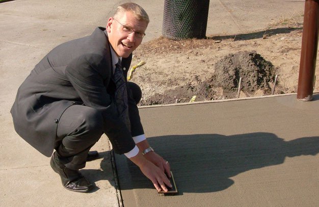 Kent Sunrise Rotary Club President Dean Saggau installs an ADA plaque on the sand table at Lake Meridian Park.