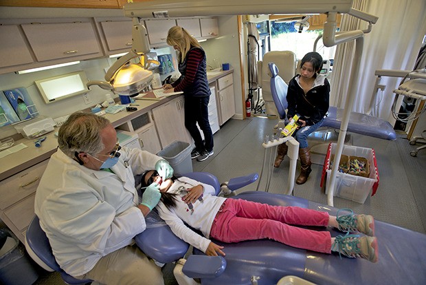 Dr. Paul Phillips examines Aiko Nguyen’s teeth on the SmileMobile mobile dental office at Kent Elementary School on Monday.