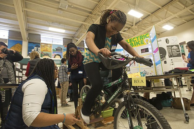 Confidence Orji from the TAF Academy demonstrates the electric bike she created with a teammate. The bike uses a wheel hooked to a generator to create energy from cycling. More than 100 independent projects by innovative young scientists were displayed at the annual TAF (Technology Access Foundation) Academy STEM Expo