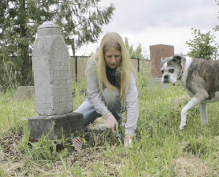Karen Bouton pulls the weeds of of J.H.S Johnson’s headstone with her watchdog Emma by her side.  Bouton is a volunteer at Saar Pioneer Cemetery and a member of the South King County Genealogical Society