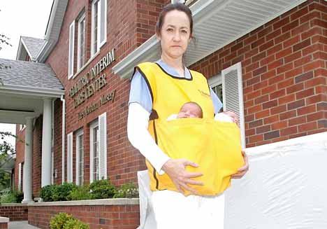 Nurse Aid Katy Bohm walks Tuesday with a infant emergency-evacuation apron carrying a baby girl