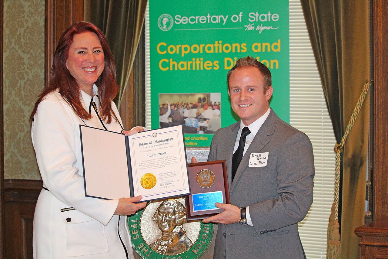Secretary of State Kim Wyman congratulates Jarrett Tomalin, community relations supervisor at Sleep Train, during a recent ceremony. The Kent-based mattress company earned the Corporations for Communities Award for its work in the community. COURTESY PHOTO