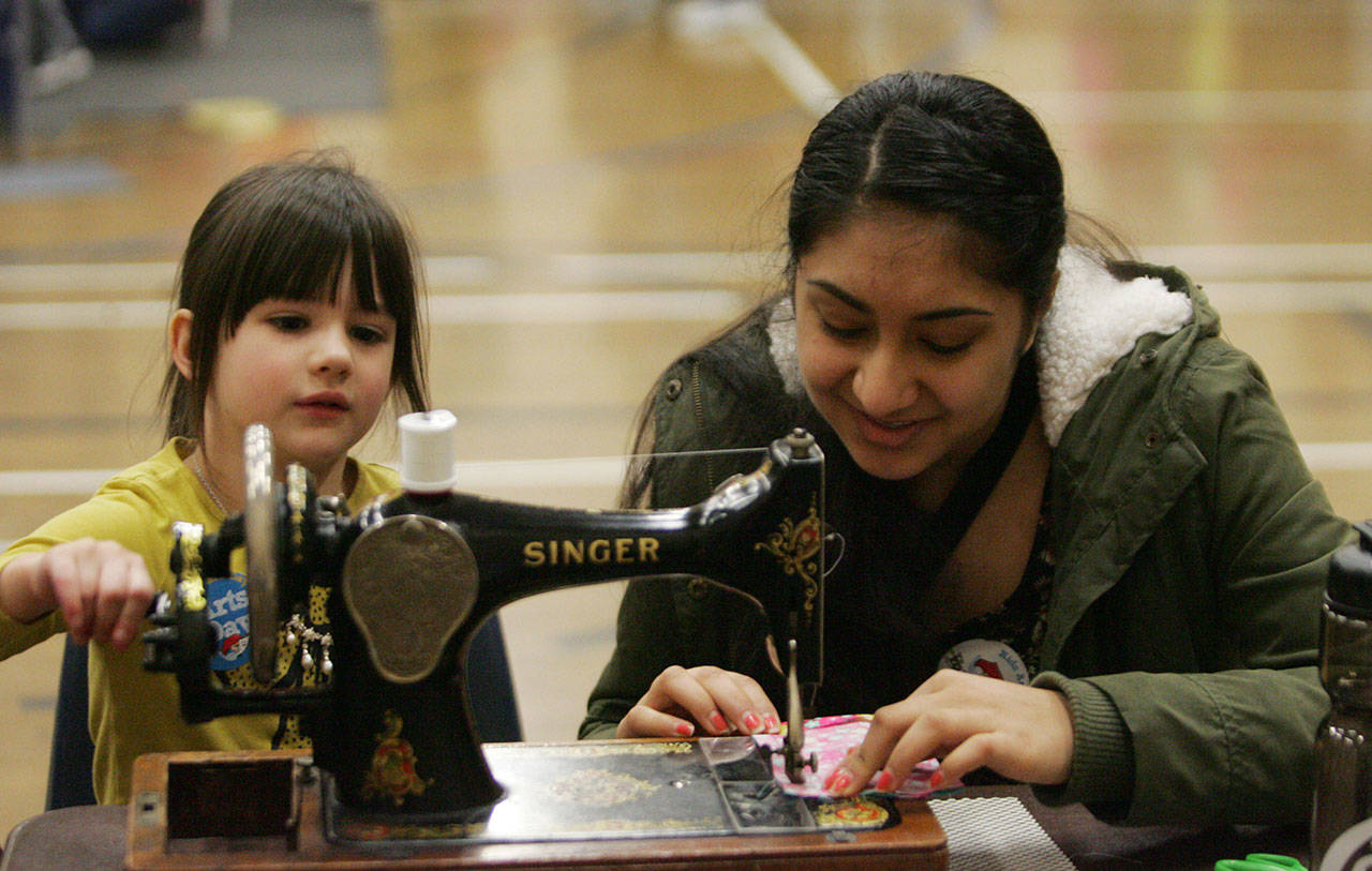 Kentwood High School student Harneet Manai shows Cambrie Smith, 4, how to sew.