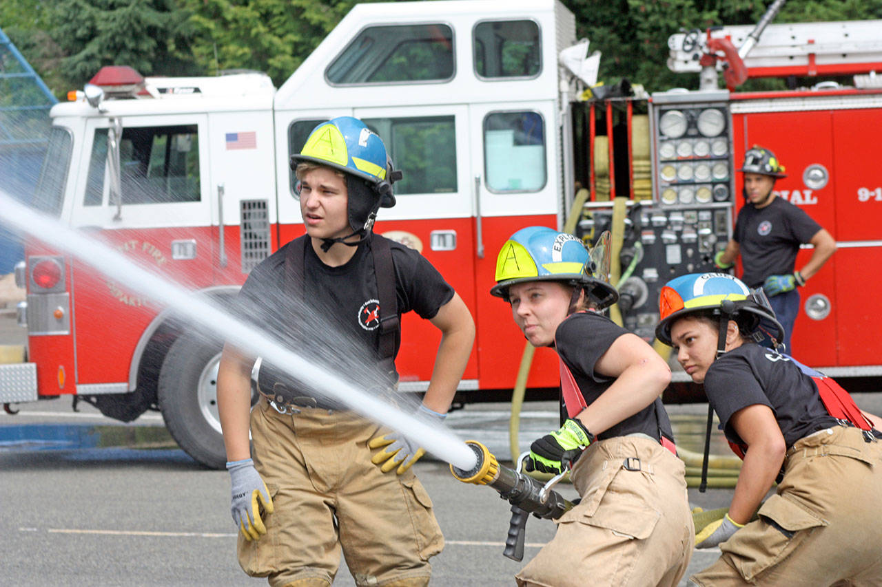 As Garrett Gregson leads, Cassie Stewart and Kehaulani Planesi work the hose during a drill last Friday at the Puget Sound Regional Fire Authority’s Summer Fire School. Firefighter and instructor Marvin Oakcrum mans the controls. MARK KLAAS, Kent Reporter
