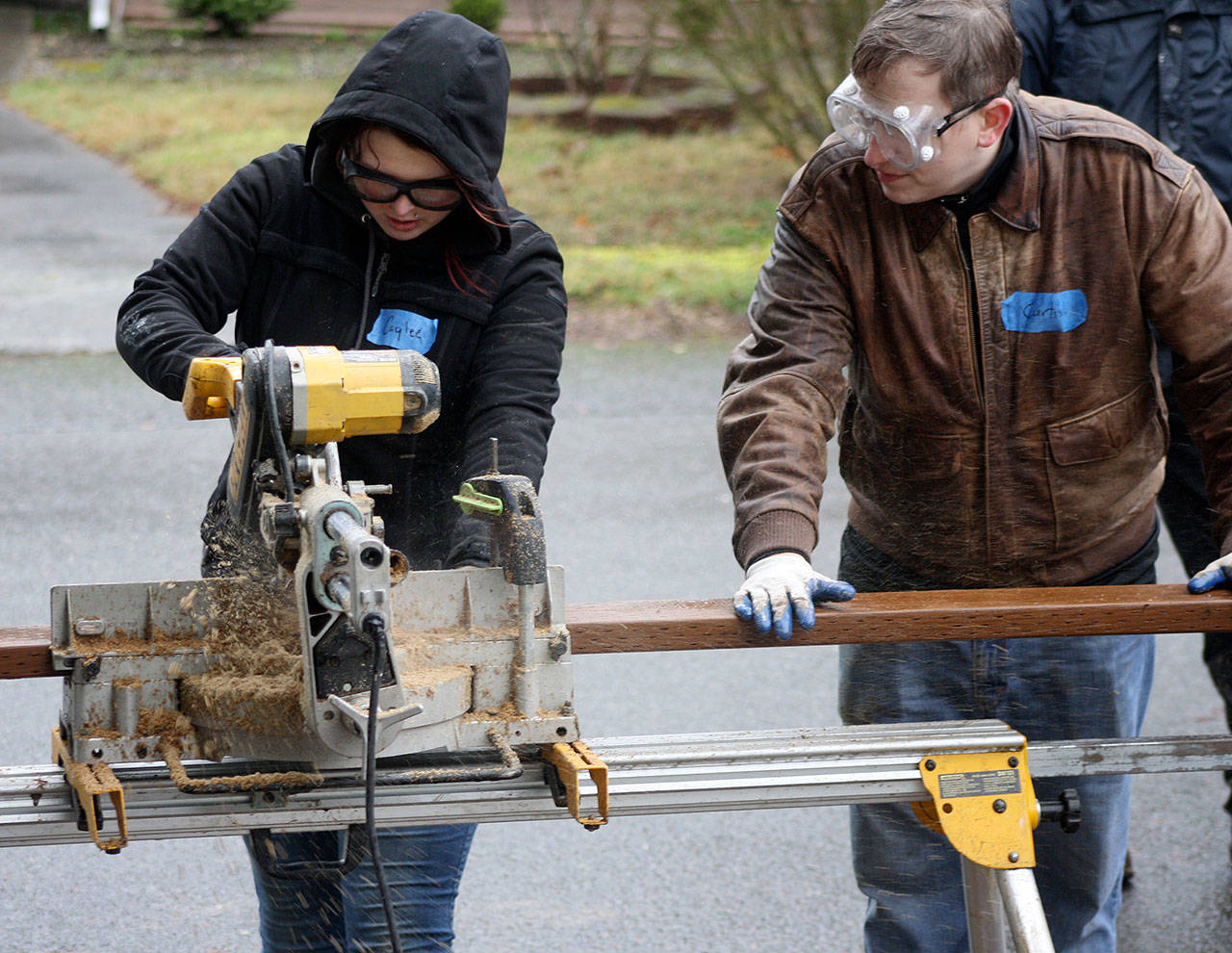 Caylee Kearns, left, cuts a board last Friday for a new deck as Curtiss Nelson assists. Both are among several volunteers from Wells Fargo helping to redo steps, install a ramp and build a deck for military veteran Lina Paulgen at her East Hill home in Kent. STEVE HUNTER, Kent Reporter