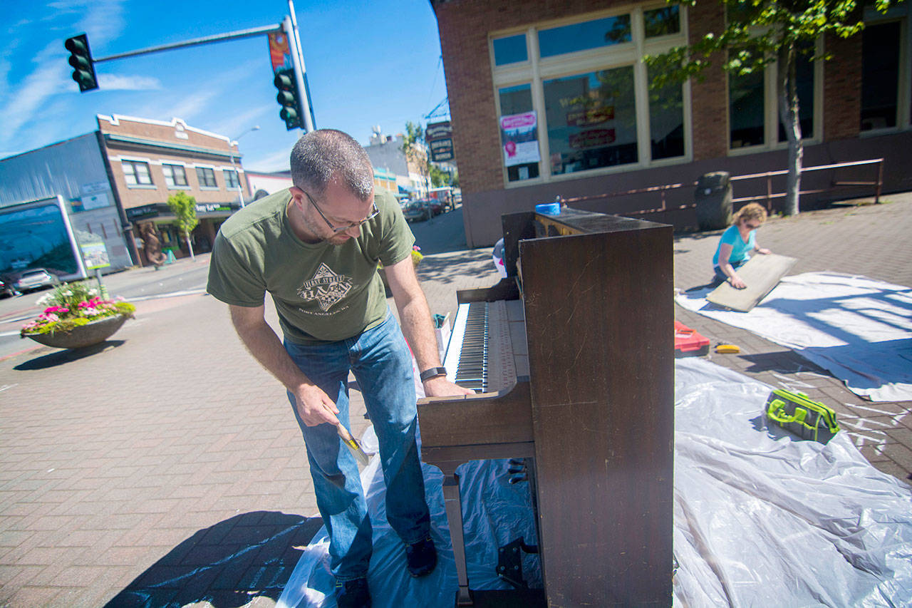 Port Angeles Council member and downtown business owner Mike French works on a piano, which he started putting out downtown during sunny days last year, during a work party on Saturday. (Jesse Major/Peninsula Daily News)