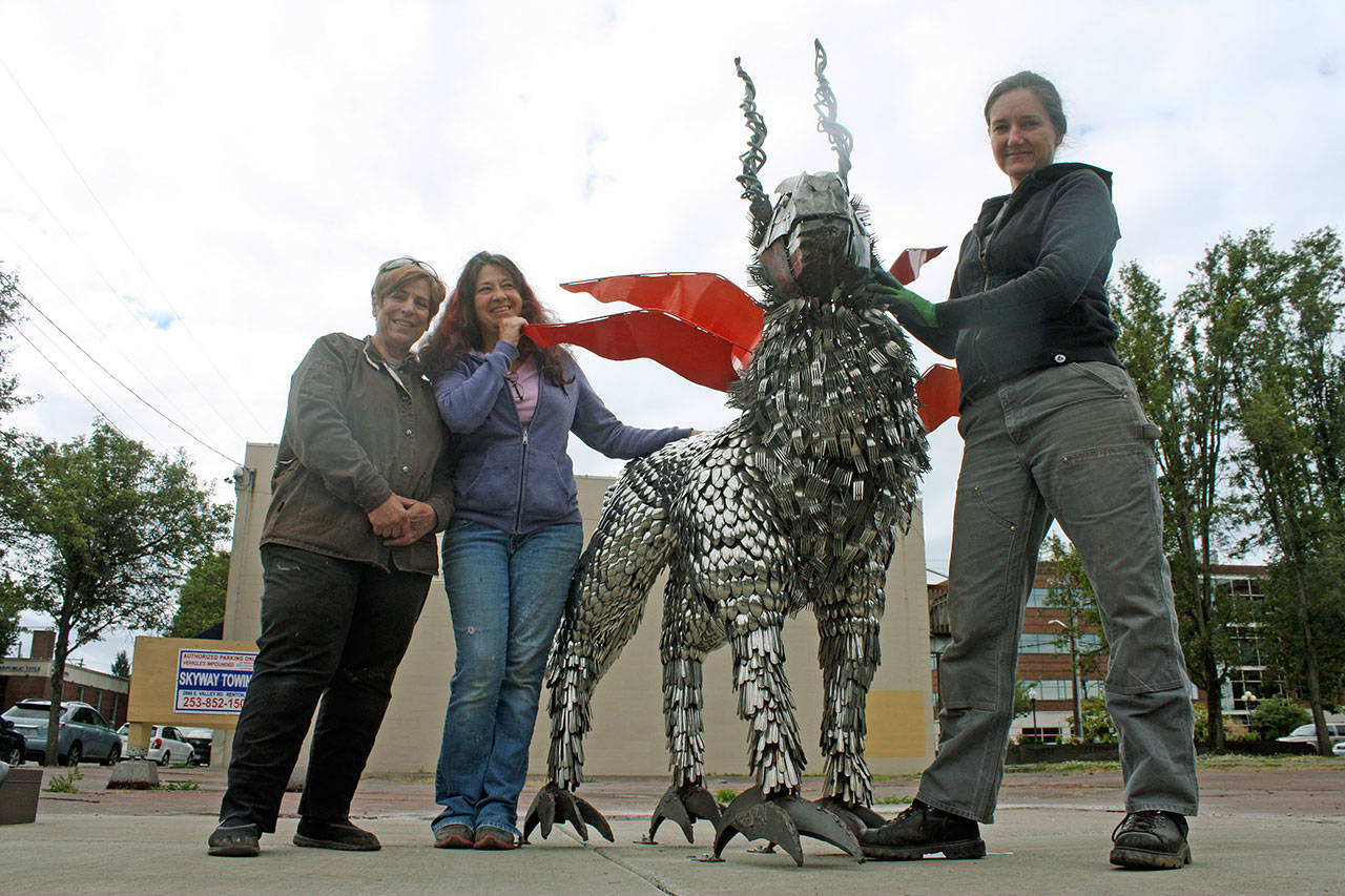Local independent artists, from left, Anita Schuller, Debbie Drllevich and Jenifer Wright introduce The Guardian, a mystical creature art sculpture, during the installation in downtown Kent last week. MARK KLAAS, Kent Reporter