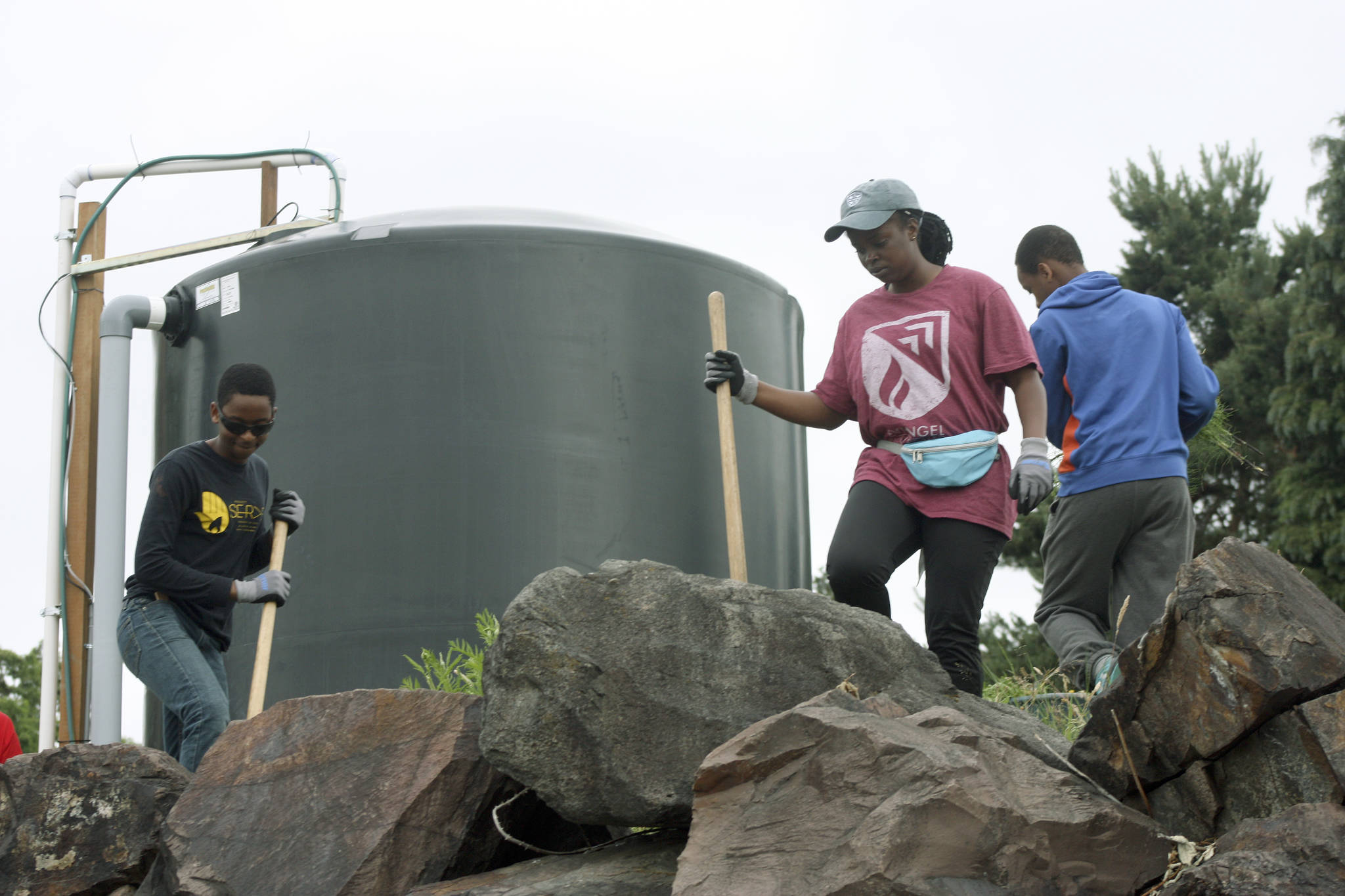 Aimee Ingabire, middle, who immigrated from the Congo Republic, and youth from the Hillside Church 
weed around one of the cisterns at the Paradise Parking Plots Community Garden last Saturday.                                 MARK KLAAS, Kent Reporter