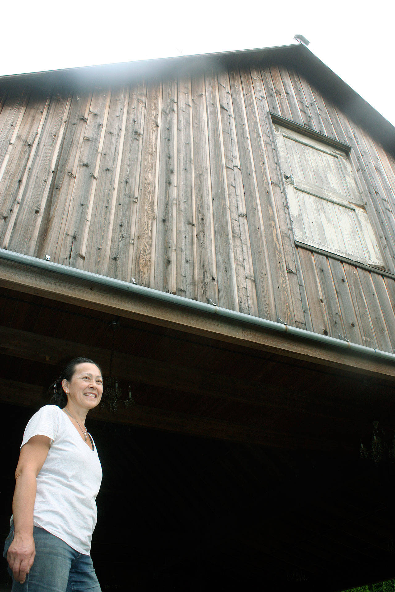 Linda Person looks on from the base of the Sidetrack Distillery Barn, built from the design and materials of historical barns in the Green River Valley. Doors recovered from a late-1800 barn grace the building. The Persons own and operate the barn as a venue for public events, along with the Lazy River Farm that feeds their small distillery. MARK KLAAS, Kent Reporter