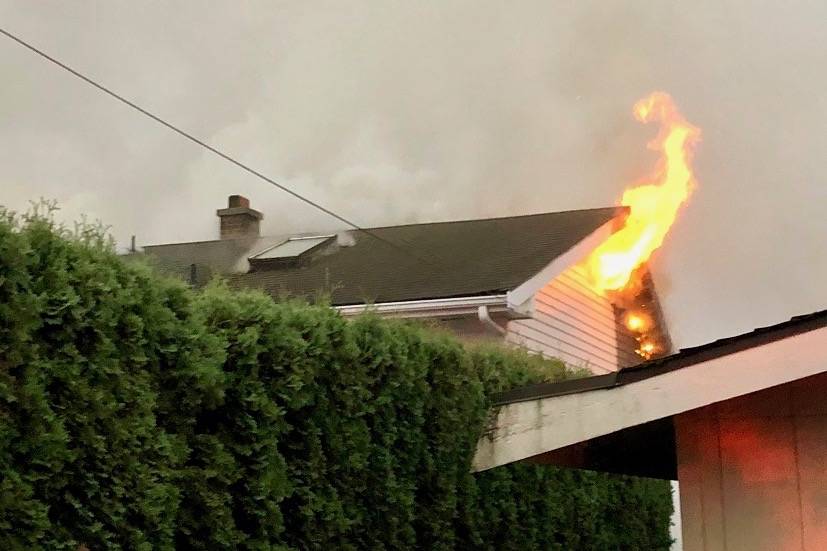 Fire spews from the attic of one of the two homes damaged in a blaze in the 14200 block of Southeast 264 Street early Saturday. COURTESY PHOTO, Puget Sound Fire