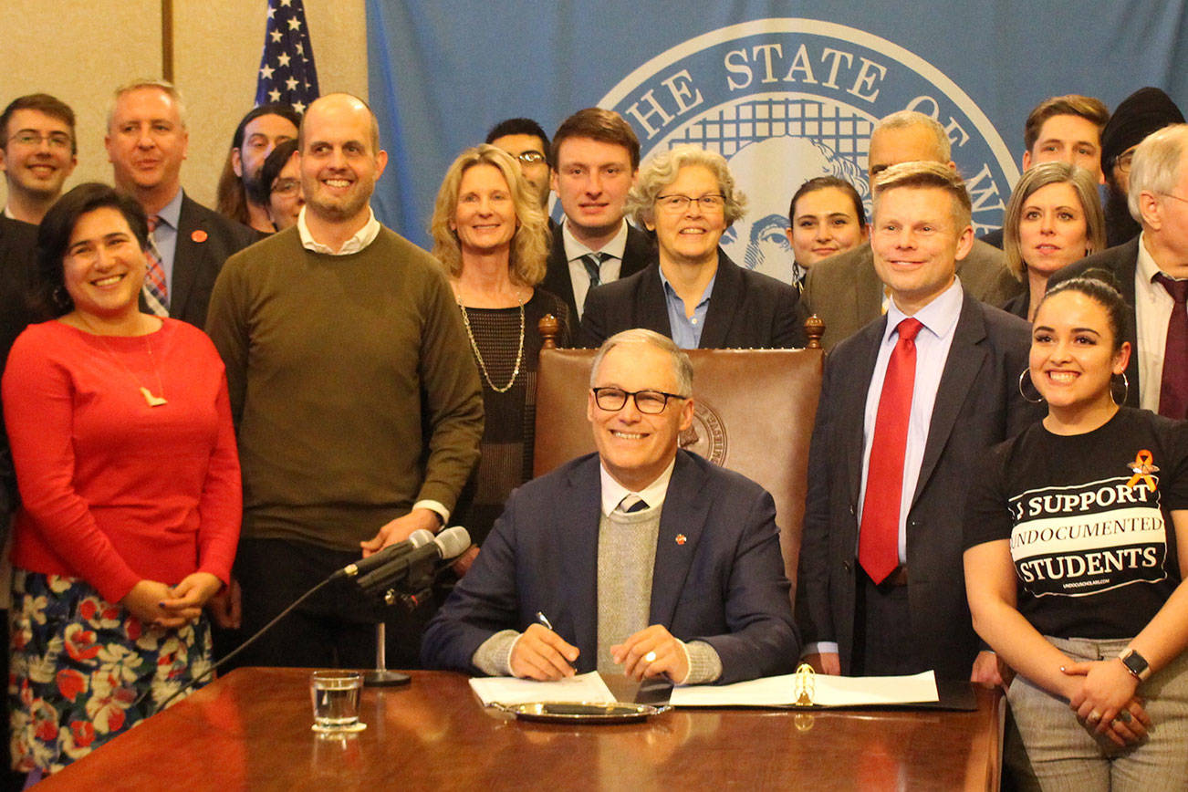 Gov. Jay Inslee signs the first bill of the 2020 legislative session into law. On the right stands the bills primary sponsor, Sen. Jamie Pedersen, D-Seattle, who is wearing a red tie. Photo by Cameron Sheppard, WNPA News Service