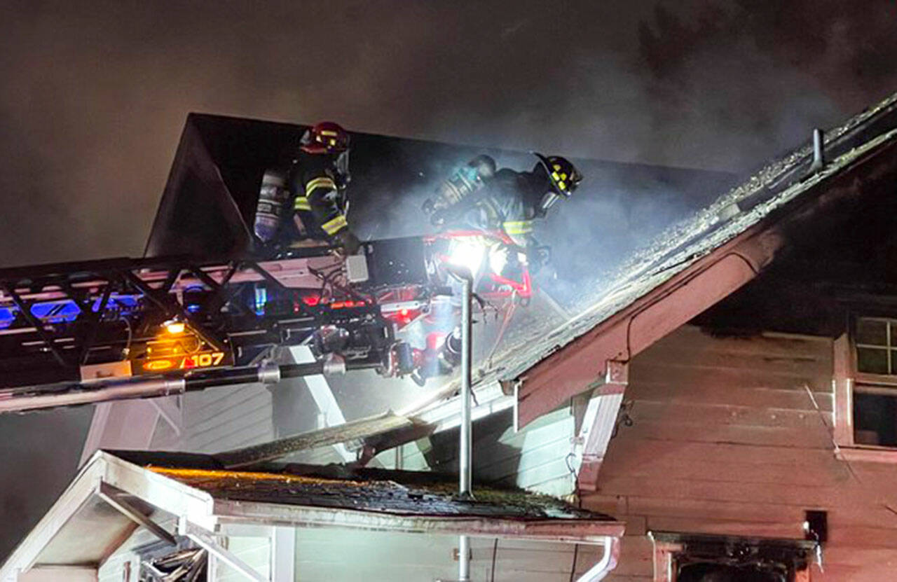Firefighters scramble up a ladder truck to combat a fire at a vacant Kent home. COURTESY PHOTO, Puget Sound Fire