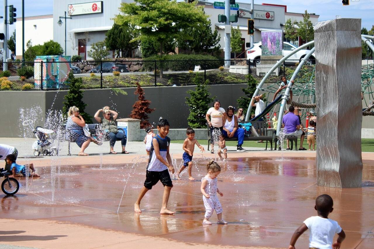 Families splash and play in the water at at Federal Way’s Town Square Park to cool off from a previous heatwave in the region. (File photo)