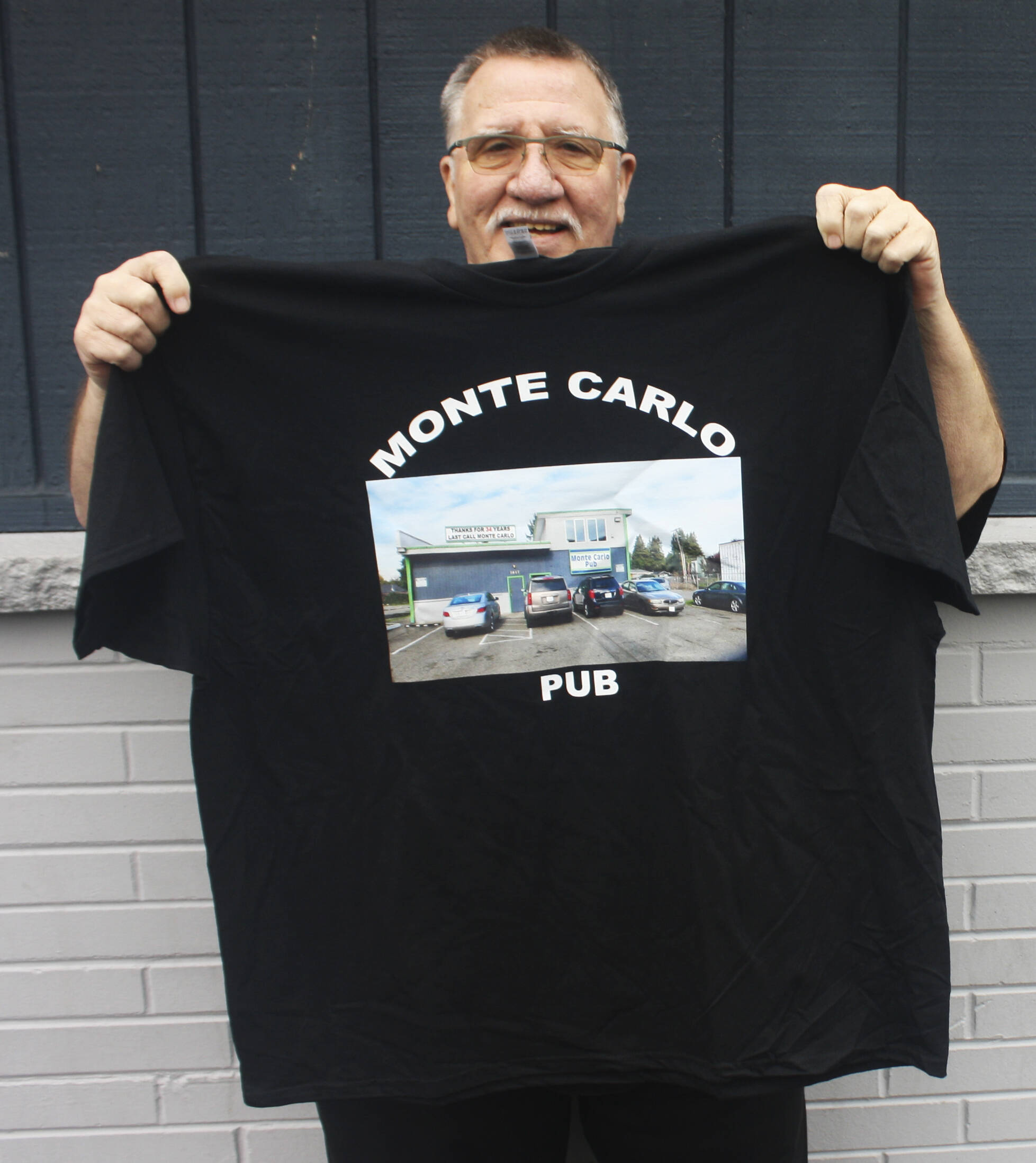 Monte Carlo Pub owner Jeff Kohler holds up a T-shirt honoring the 34 years the bar’s been in business in Kent along West Meeker Street. STEVE HUNTER, Kent Reporter