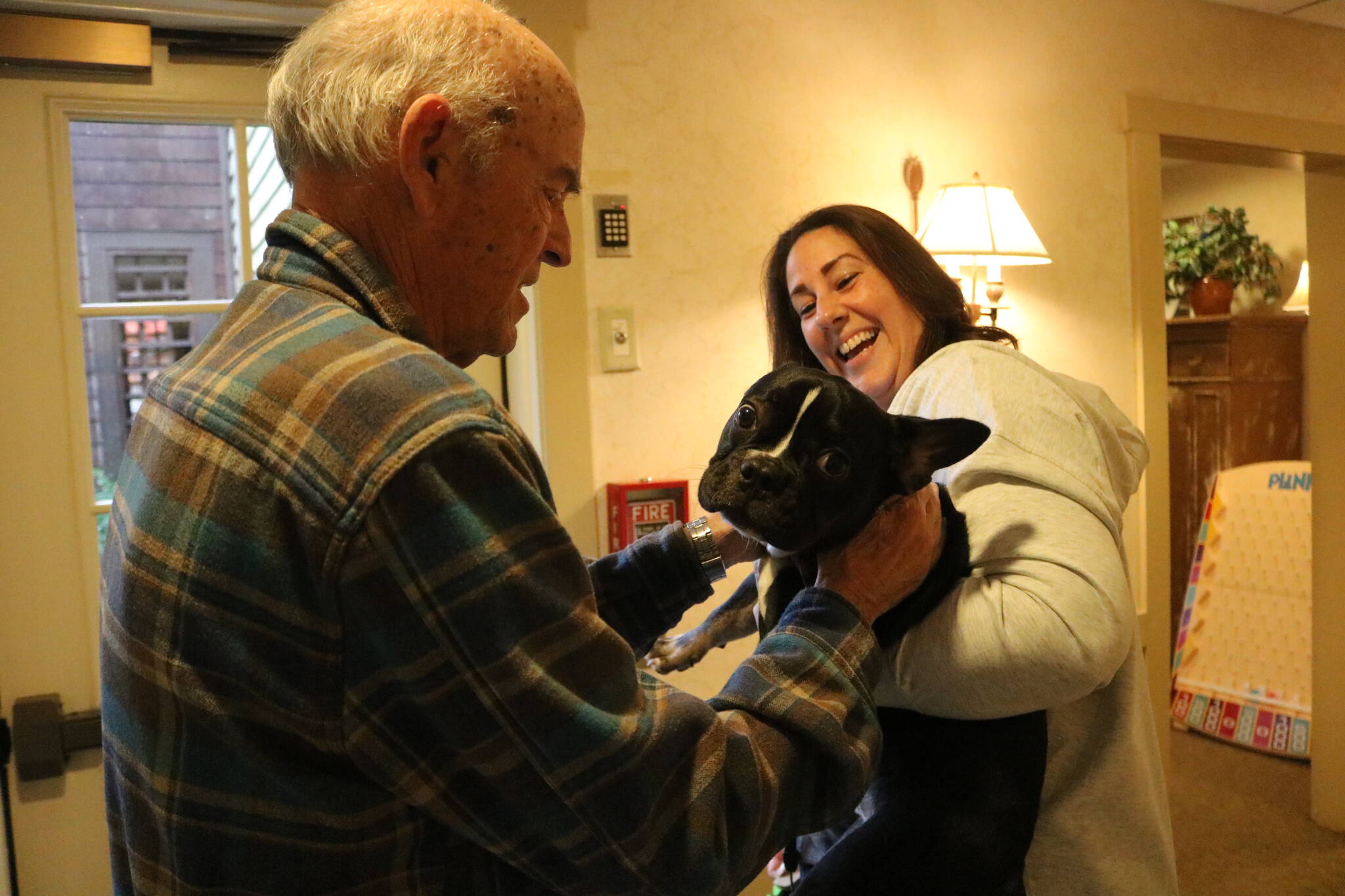 Weatherly Inn general manager Sabrina Selden holds Milo the house dog in-training so that a resident can give him some pets. Photo by Bailey Jo Josie/Sound Publishing.