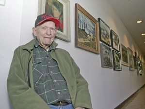 Kent artist Danny Pierce sits below a self-portrait of himself at about 25 years old at the Centennial Center Gallery on Sept. 2