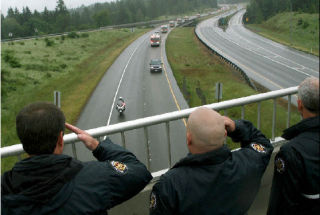 Auburn’s Valley Regional Fire Authority firefighters salute as the family of Kent firefighter Marty Hauer travels Tuesday under the South 304th Street bridge along Highway 18.