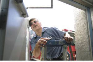 Steve Pinto gets a closer look at screws that control latch speed on a door that was sticking at Fire Station 72 Wednesday.