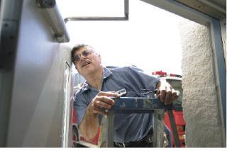 Steve Pinto gets a closer look at screws that control latch speed on a door that was sticking at Fire Station 72 Wednesday.