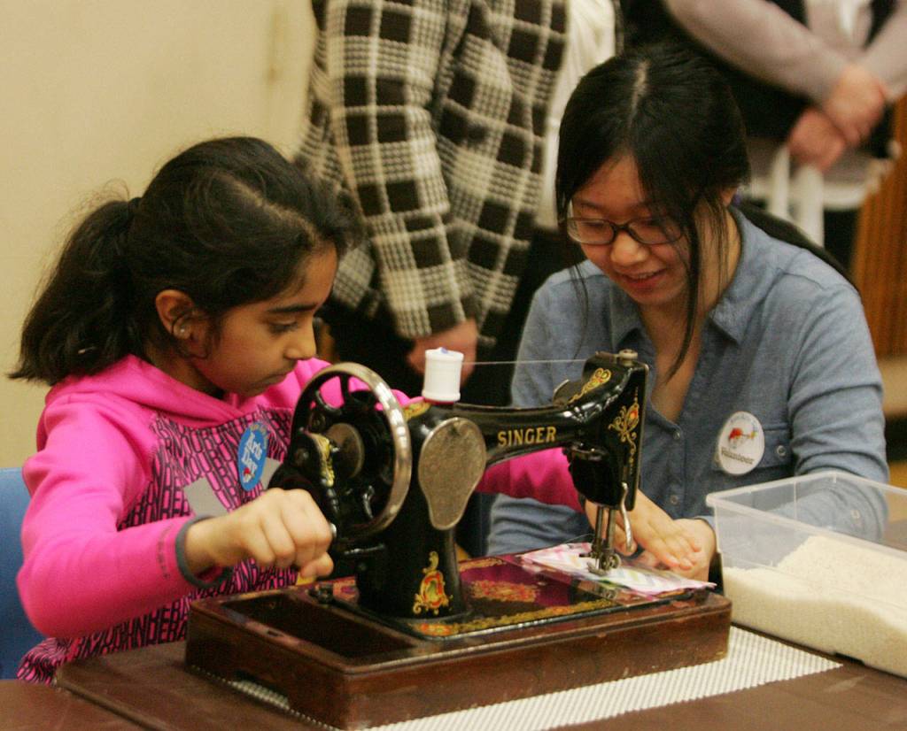 Kent-Meridian High School student Diane Yeyat helps Navya Parmar, 9, sew. DENNIS BOX, Reporter