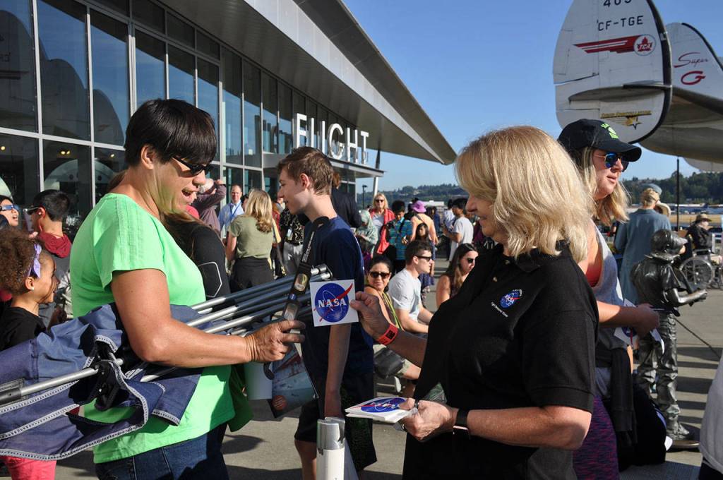 Leslie Williams, news chief for the NASA Armstrong Flight Research Center, right, gives NASA stickers to eclipse-goers at the Museum of Flight. HEIDI SANDERS, Reporter