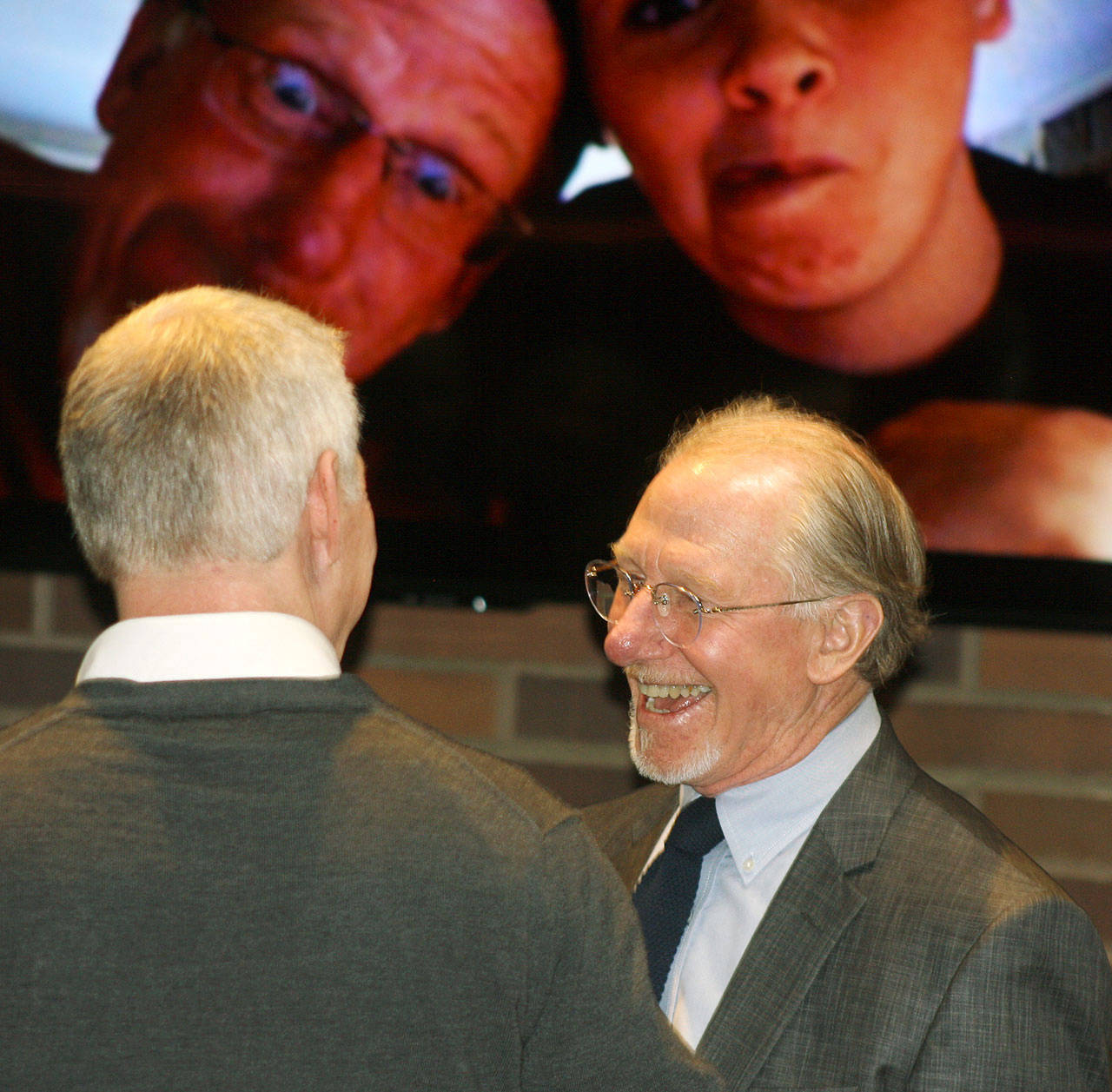Retiring Kent City Attorney Tom Brubaker, right, chats with Tim Higgins, accesso ShoWare Center general manager, during a farewell party Thursday in Council Chambers at City Hall. A photo display of Brubaker ran on the flat screen behind him. STEVE HUNTER, Kent Reporter