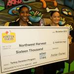 Jasmine Bridges, corporate engagement officer for Northwest Harvest, and Maritza Prince, food drive-operations coordinator for NW Harvest, accept a $16,000 check from Foster Farms for the turkey donation program on Tuesday.