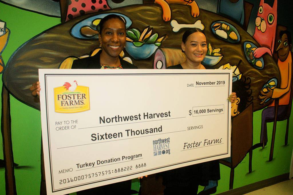 Jasmine Bridges, corporate engagement officer for Northwest Harvest, and Maritza Prince, food drive-operations coordinator for NW Harvest, accept a $16,000 check from Foster Farms for the turkey donation program on Tuesday.