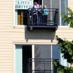 A family hangs a poster from The Platform Apartments and watches the Black Lives Matter protest march June 11 in downtown Kent. STEVE HUNTER, Kent Reporter
