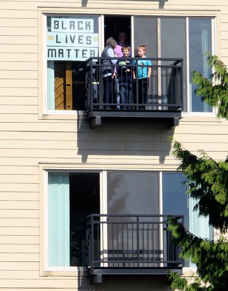 A family hangs a poster from The Platform Apartments and watches the Black Lives Matter protest march June 11 in downtown Kent. STEVE HUNTER, Kent Reporter