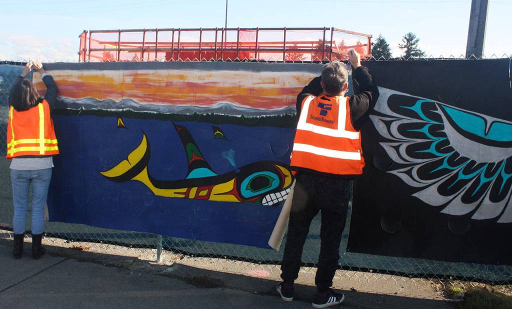 Sound Transits Lucile Chich and Tim Marsden install a mural on the light rail construction fencing along Pacific Highway South. STEVE HUNTER, Kent Reporter