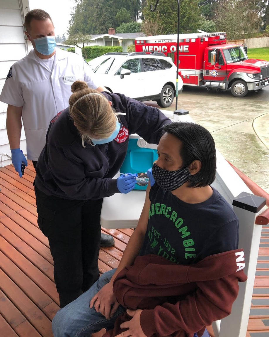 Nurse Sara Hardin, part of Puget Sound Fires first COVID-19 mobile vaccination unit, delivers a shot Jan. 21 to a resident at an adult family home in Kent. Kyle Waterman, a King County Medic One paramedic, looks on. COURTESY PHOTO, Puget Sound Fire