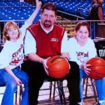 Aly Carr (left) and Cait Carr (far right) sit with their father Chris Carr (center) on the sidelines of a basketball court in 2003. The sisters watched their father coach at various high schools growing up, which later inspired them to become high school basketball coaches themselves. (Photo courtesy of Marla Carr)