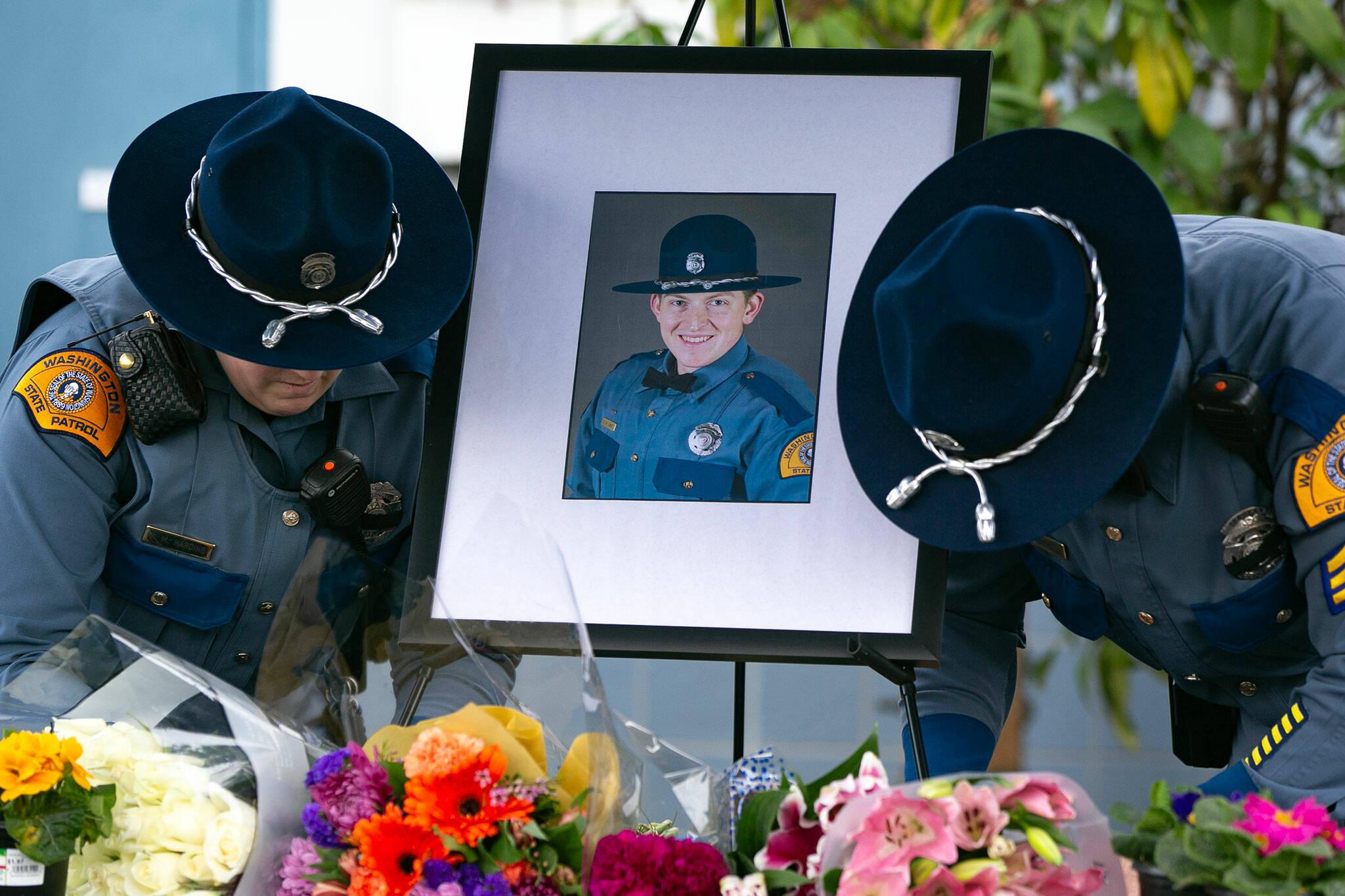 Two troopers place a photo of their slain colleague, Chris Gadd, outside state patrols District 7 Headquarters about twelve hours after Gadd was struck and killed on southbound I-5 about a mile from the headquarters on Saturday, March 2, 2024, in Marysville, Washington. (Ryan Berry / The Herald)