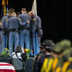 A group of Washington State Trooper Chris Gadds closest friends and coworkers add a ribbon baring his name to the Washington State Patrol flag on Tuesday, March 12, 2024, at Angel of the Winds Arena in Everett, Washington. (Ryan Berry / The Herald)