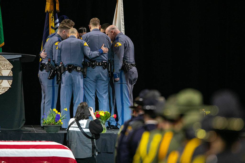 A group of Washington State Trooper Chris Gadds closest friends and coworkers add a ribbon baring his name to the Washington State Patrol flag on Tuesday, March 12, 2024, at Angel of the Winds Arena in Everett, Washington. (Ryan Berry / The Herald)