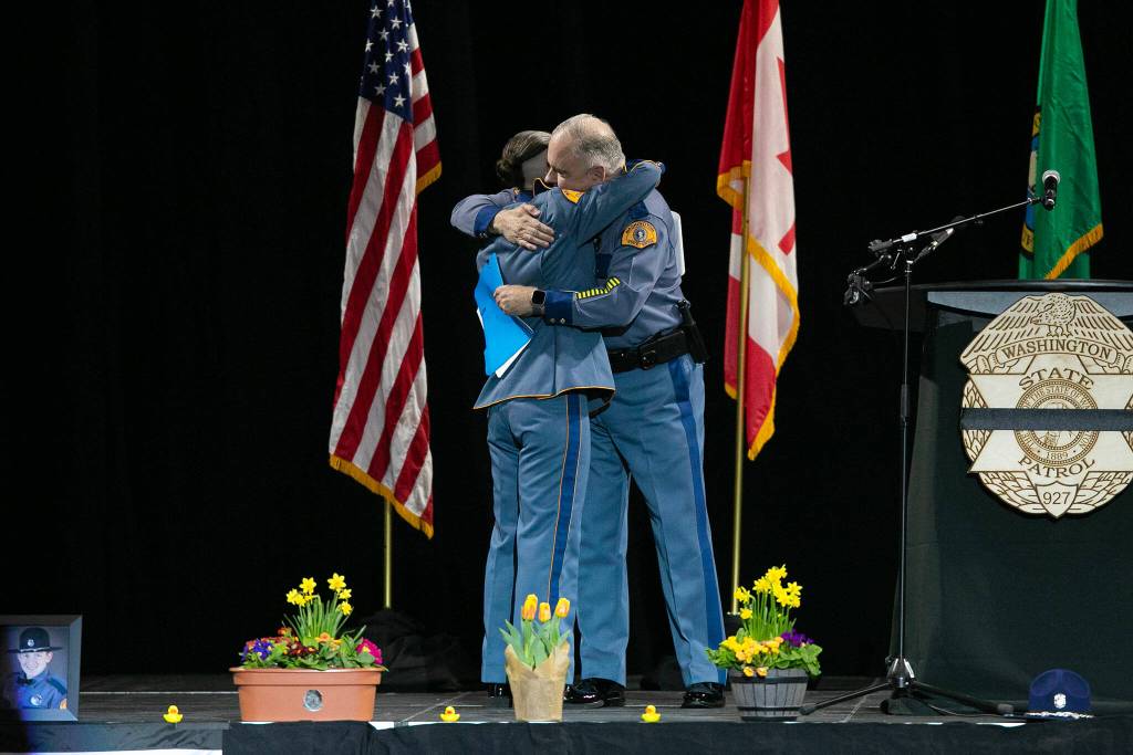 Captain Ron Mead and Corporal Alexis Robinson embrace during a memorial for Washington State Trooper Chris Gadd on Tuesday, March 12, 2024, at Angel of the Winds Arena in Everett, Washington. (Ryan Berry / The Herald)