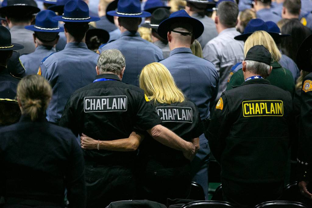 Chaplains and other members of the crowd listen as Taps is played during a memorial for Washington State Trooper Chris Gadd on Tuesday, March 12, 2024, at Angel of the Winds Arena in Everett, Washington. (Ryan Berry / The Herald)