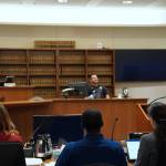 Corniche Washington is in the middle, wearing a blue shirt between his counsel, while prosecutor Jacqueline Lawrence speaks to an officer who responded to the scene. Photo by Joshua Solorzano/The Mirror